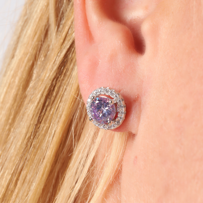 Close-up of a person wearing stunning Lavender CZ stud earrings from Mia Ishaaq, elegantly set in 925 Sterling Silver with a diamond halo setting.