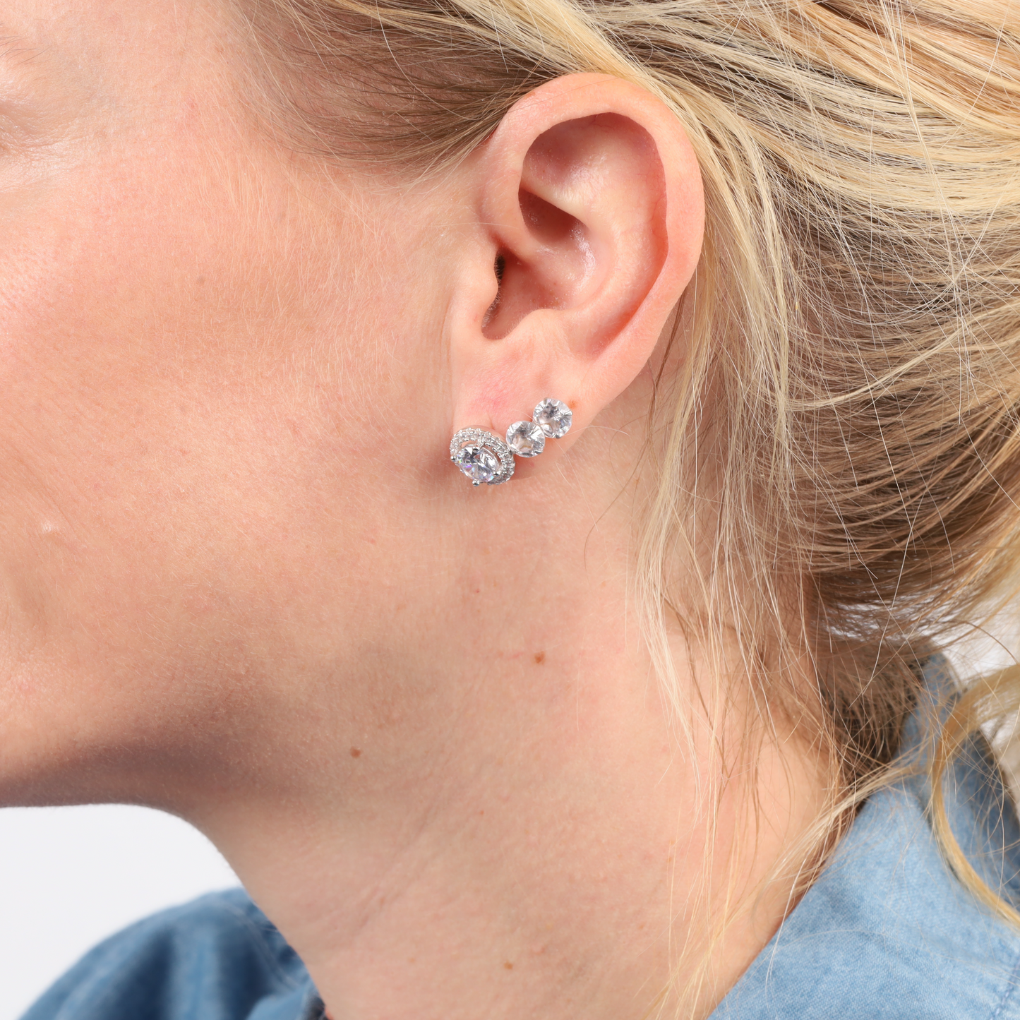 Close-up of a woman wearing Mia Ishaaq's Halo Radiance Sparkling Stud Earrings, with her hair pulled back and a blue shirt.