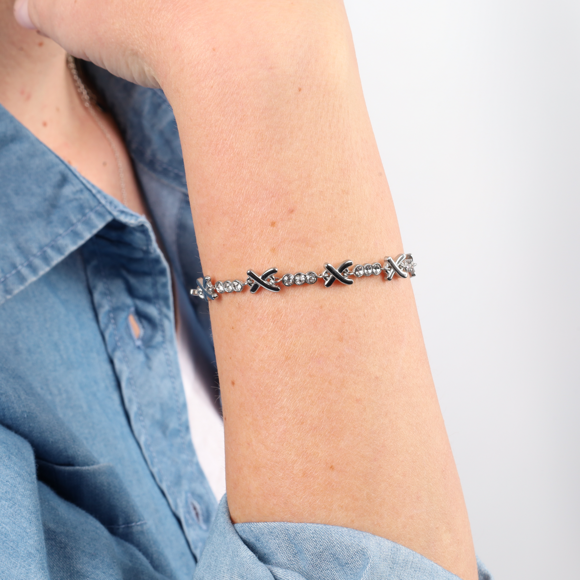 Close-up of a person wearing the Gemma Owen Inspired XO Cross Bracelet by Mia Ishaaq, featuring X-shaped and round links, dressed in a blue denim shirt.