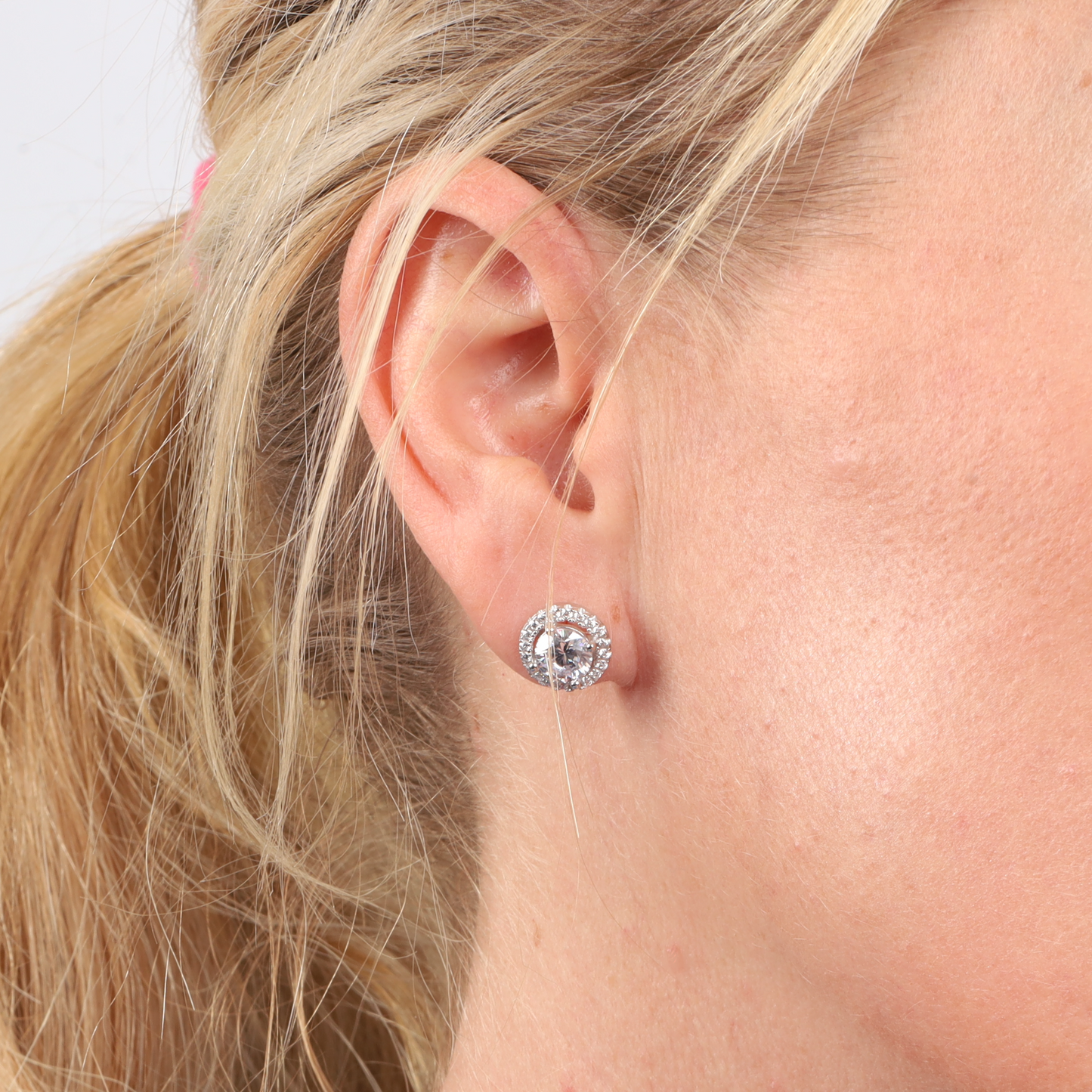 Close-up of a woman's ear adorned with the Halo Radiance Sparkling Stud Earring by Mia Ishaaq, featuring a sparkling round diamond crafted from 925 sterling silver.