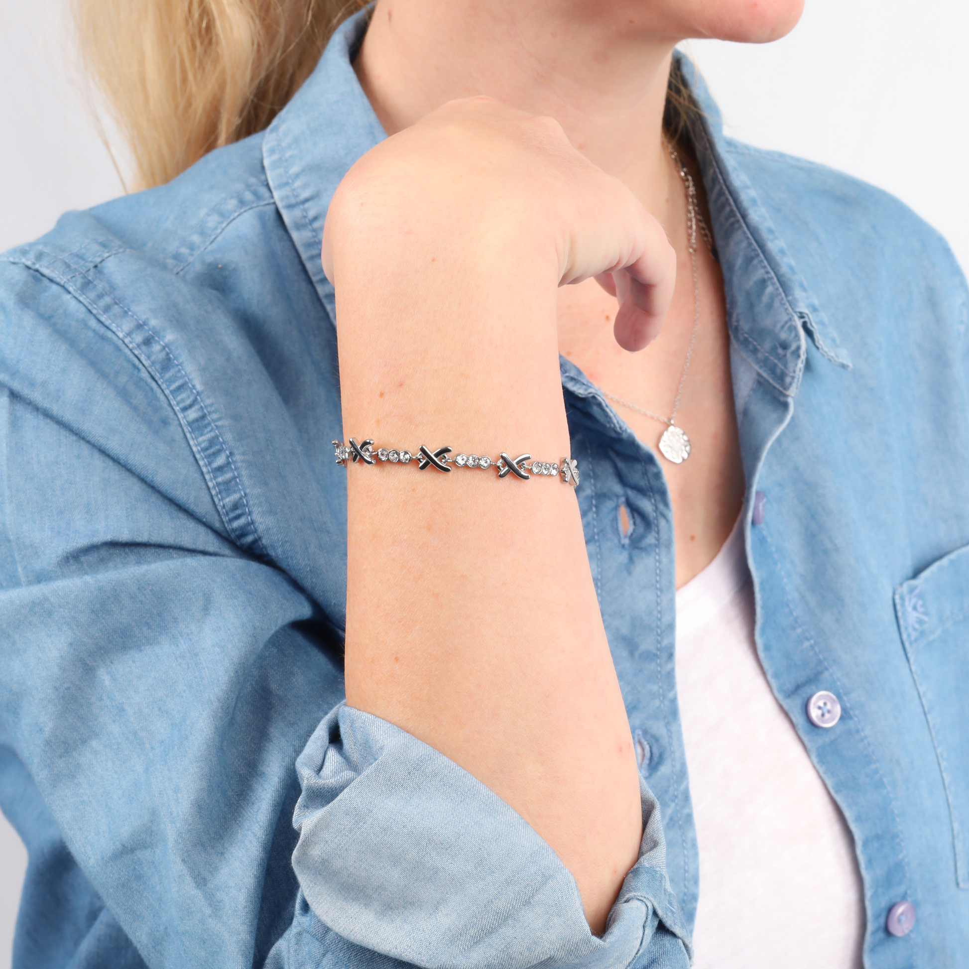 Woman in a denim shirt wearing a Mia Ishaaq Gemma Owen Inspired XO Cross Bracelet and necklace, with an arm resting near her chin.