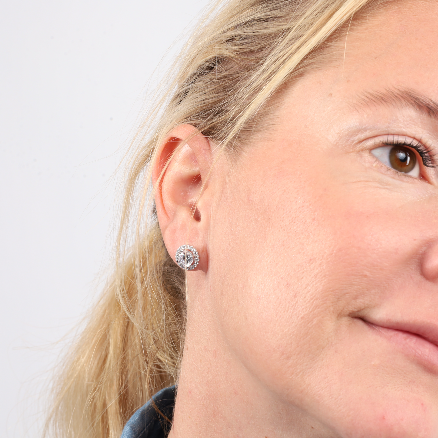 Close-up of a person wearing a light denim jacket and the Mia Ishaaq Halo Radiance Sparkling Stud Earrings, smiling slightly.