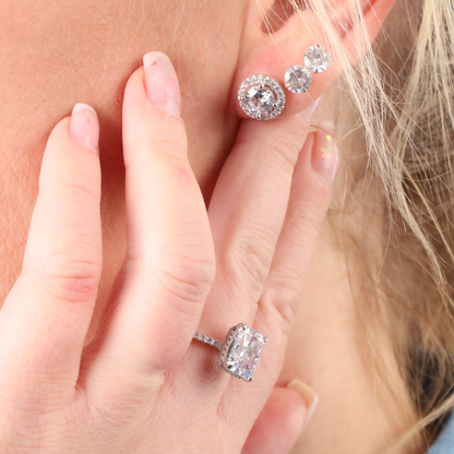 A person adorned with a Mia Ishaaq Sterling Silver Clear Radiant Ring and three earrings featuring large, round gemstones on their left ear.