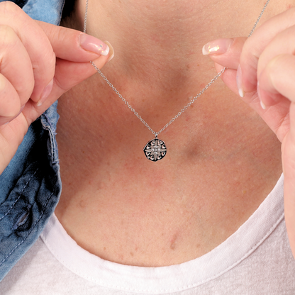 A person holds a Mia Ishaaq® Polaris Coin Pendant Necklace - Silver, its sterling silver chain glistening as it rests on a white shirt. The round pendant showcases intricate designs that capture attention and evoke the mystery of the North Star.