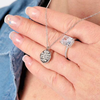 A hand adorned with a Mia Ishaaq® Polaris Coin Pendant Necklace in silver and a diamond ring, nails painted in a glittery design, wearing a denim shirt.