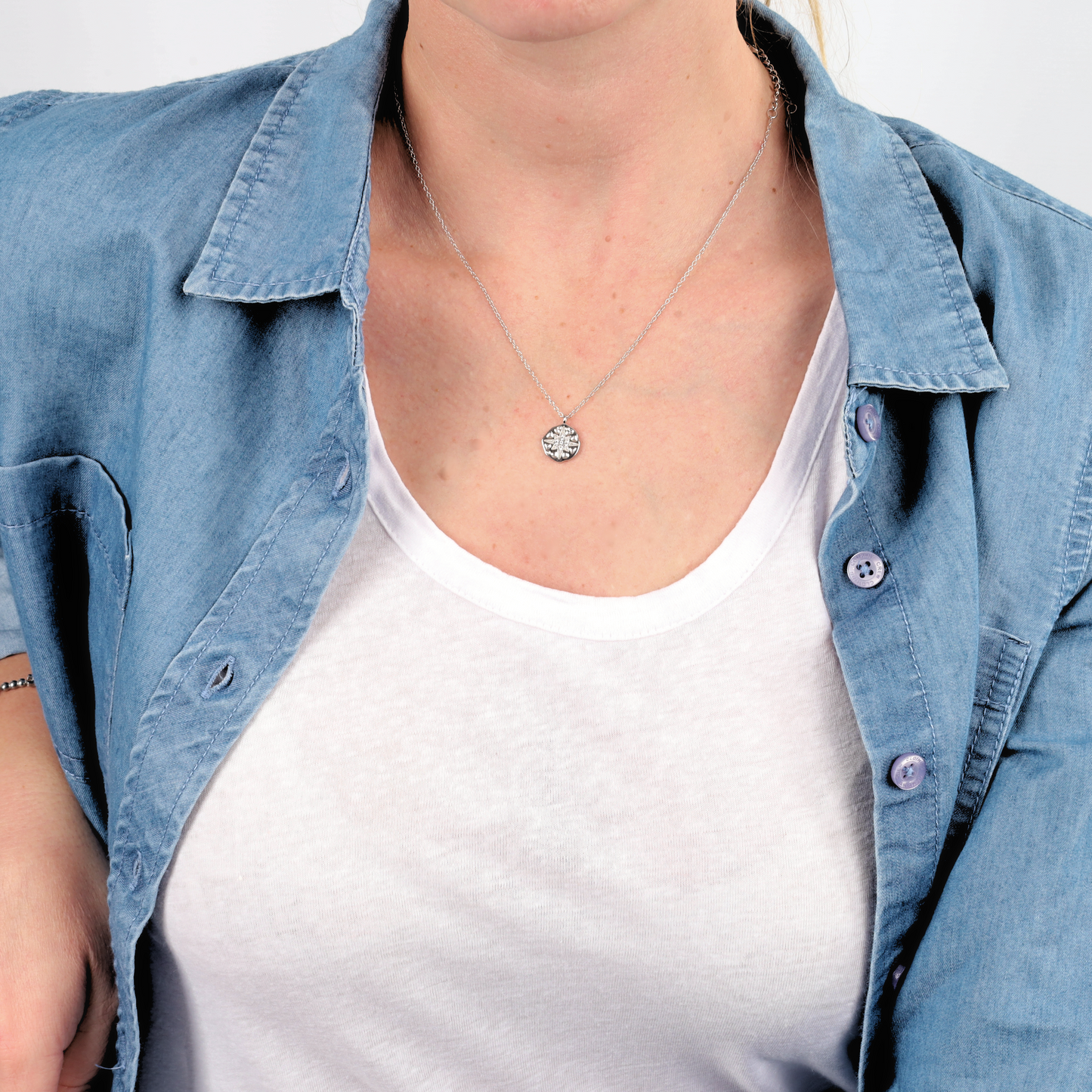 Person wearing a denim shirt over a white t-shirt, accessorized with the Silver Polaris Coin Pendant Necklace by Mia Ishaaq®.