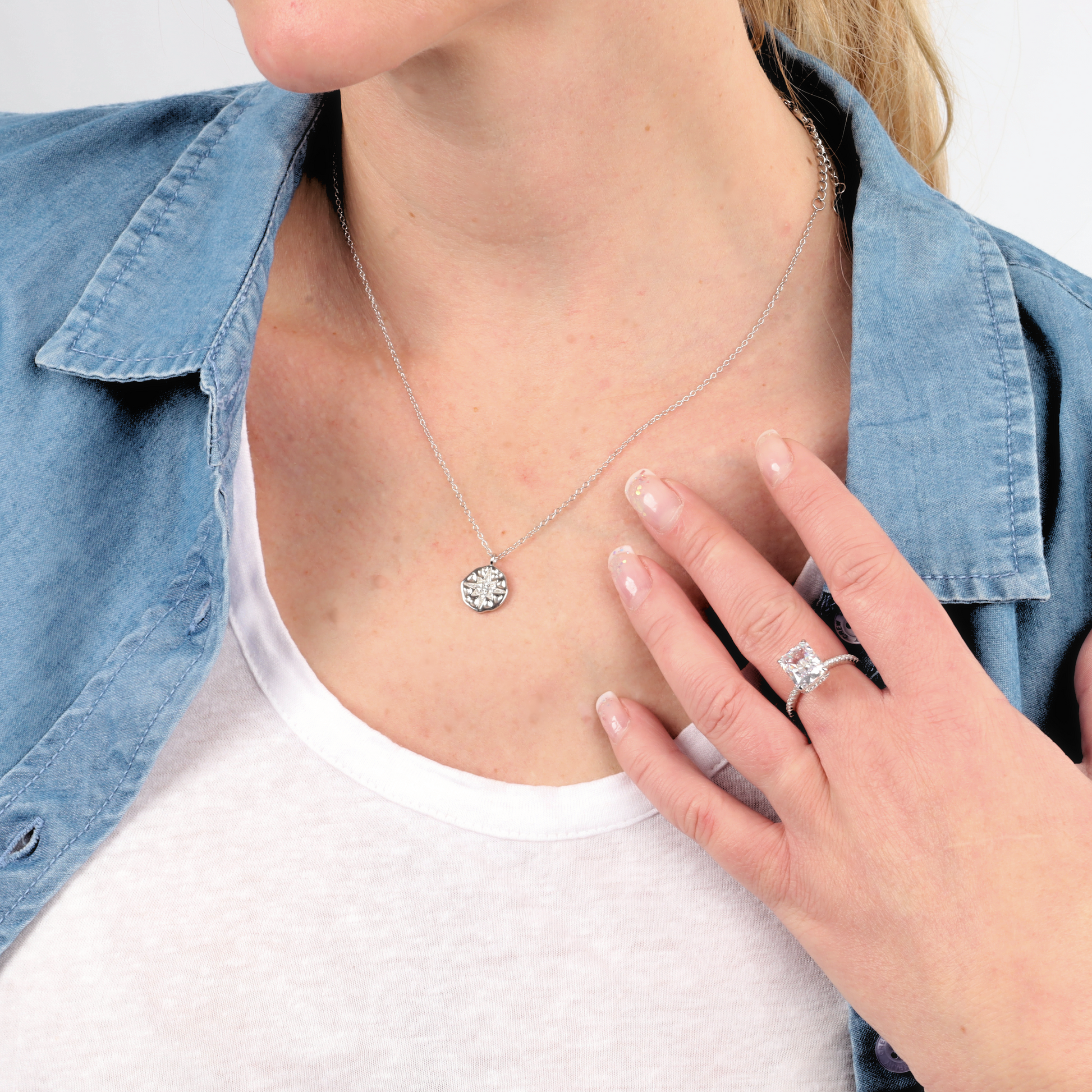 A woman accessorizes with the Sterling Silver Clear Radiant Ring by Mia Ishaaq, perfectly complementing her denim shirt worn over a white top.