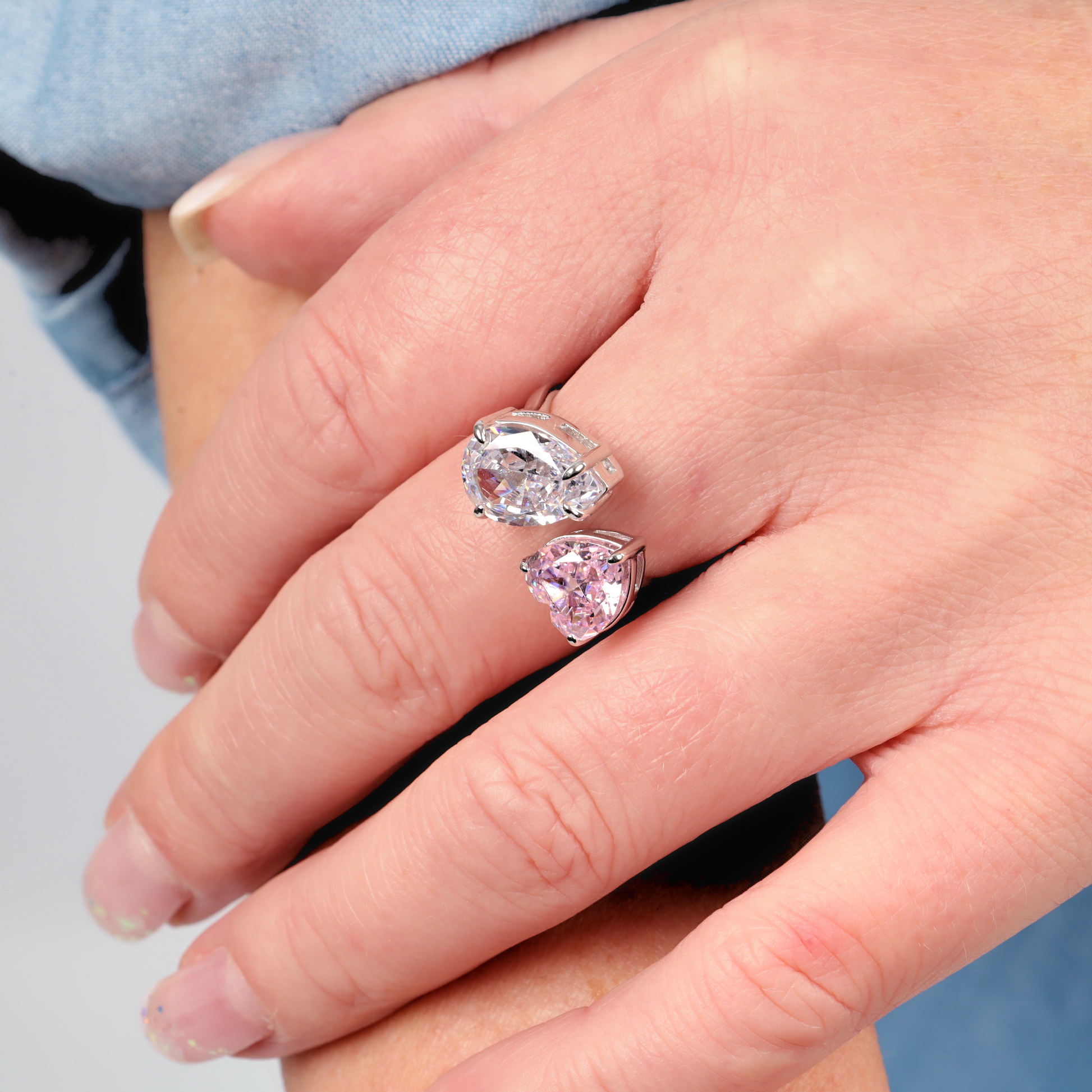 A close-up captures a hand adorned with the Mia Ishaaq Sterling Silver Radiant Duo Ring - adjustable, highlighting its modern, sleek design. The ring showcases teardrop-shaped gems—a clear gem elegantly paired with a pink hue—enhanced by the brilliance of cubic zirconia stones.