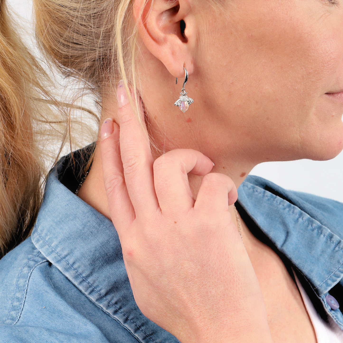 A person with blonde hair is seen wearing Mia Ishaaq's Crystal Queen Bee Dangle Earrings, touching their hair while dressed in a light blue shirt against a white background.