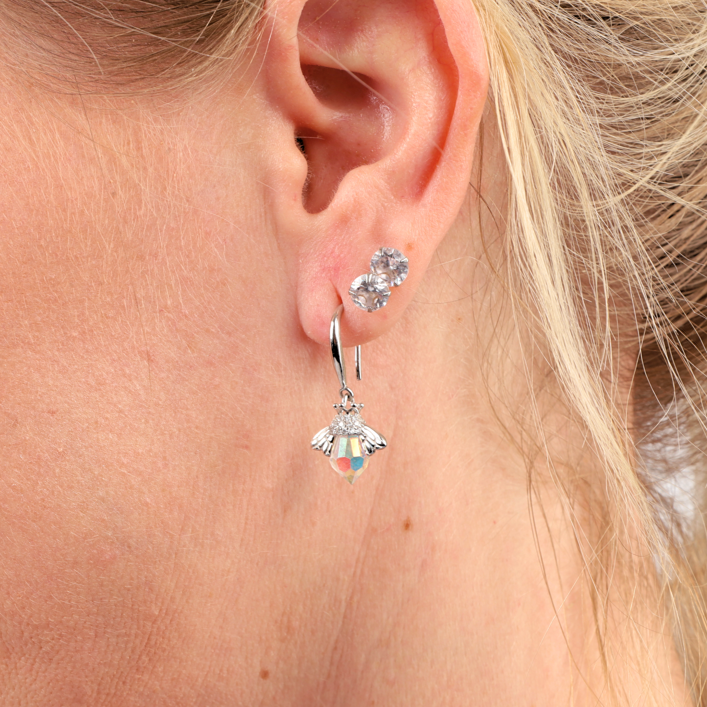 Close-up of a person's ear adorned with two Sterling Silver earrings, one a crystal stud and the other a Mia Ishaaq Crystal Queen Bee Dangle Earring.