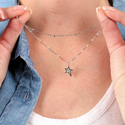 Close-up of a person holding Mia Ishaaq's Star Pendant Layered Celestial Necklace with a sterling silver design, paired with a denim shirt and white top.