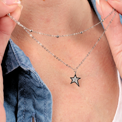 A person holding the Star Pendant Layered Celestial Necklace by Mia Ishaaq against a denim shirt.