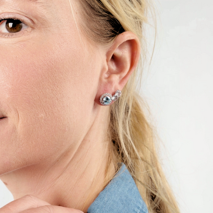 Close-up of a person wearing Mia Ishaaq's 925 Sterling Silver AQUAMARINE CZ Stud Earrings, set against a plain background.