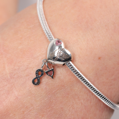 Close-up of a model's hand wearing a silver bracelet with heart-shaped dog memorial charm, showing the reverse side with winged dog and pink heart-shaped zirconia - Mia Ishaaq