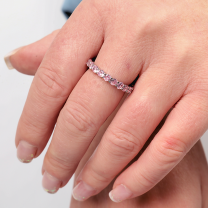 A hand adorned with a Mia Ishaaq Sterling Silver Pink Ring Band featuring a dazzling pink gemstone on the ring finger.