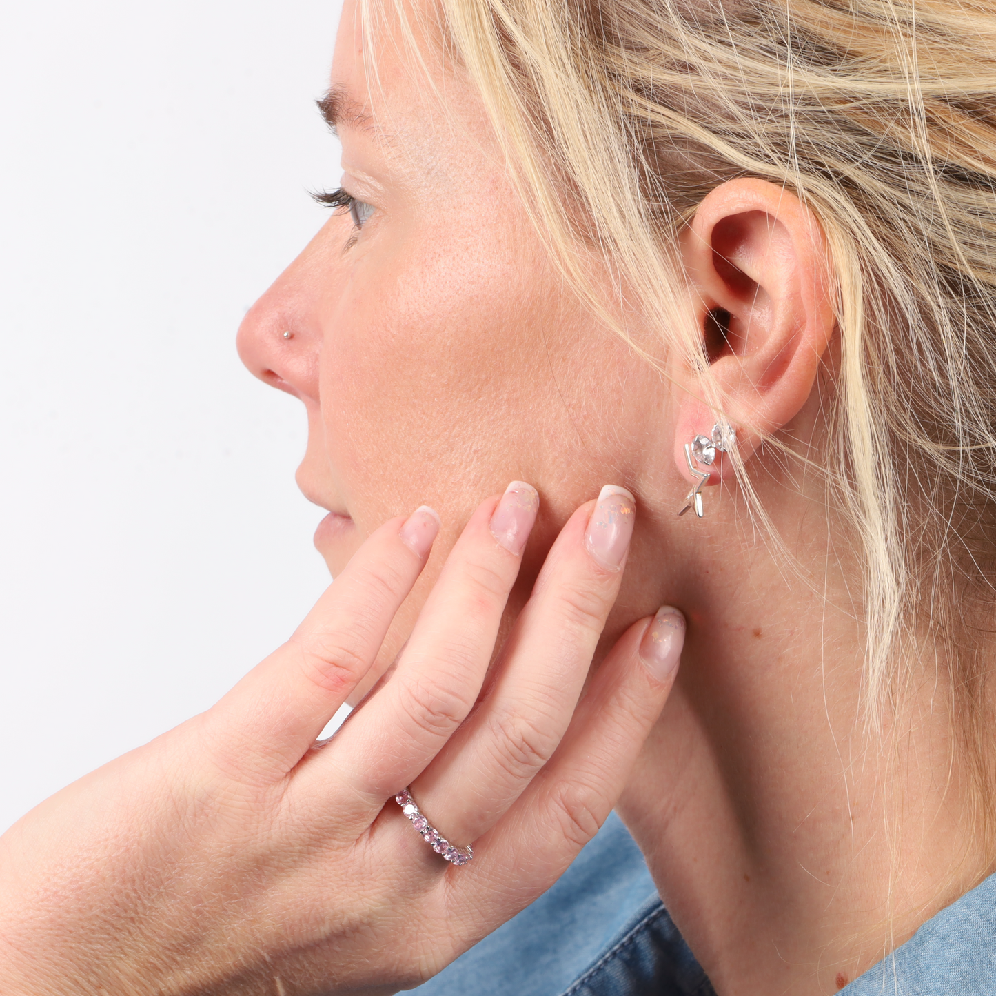 Profile view of a person with blonde hair, wearing a floral earring and the Mia Ishaaq Sterling Silver Pink Ring Band, gently touching their cheek.