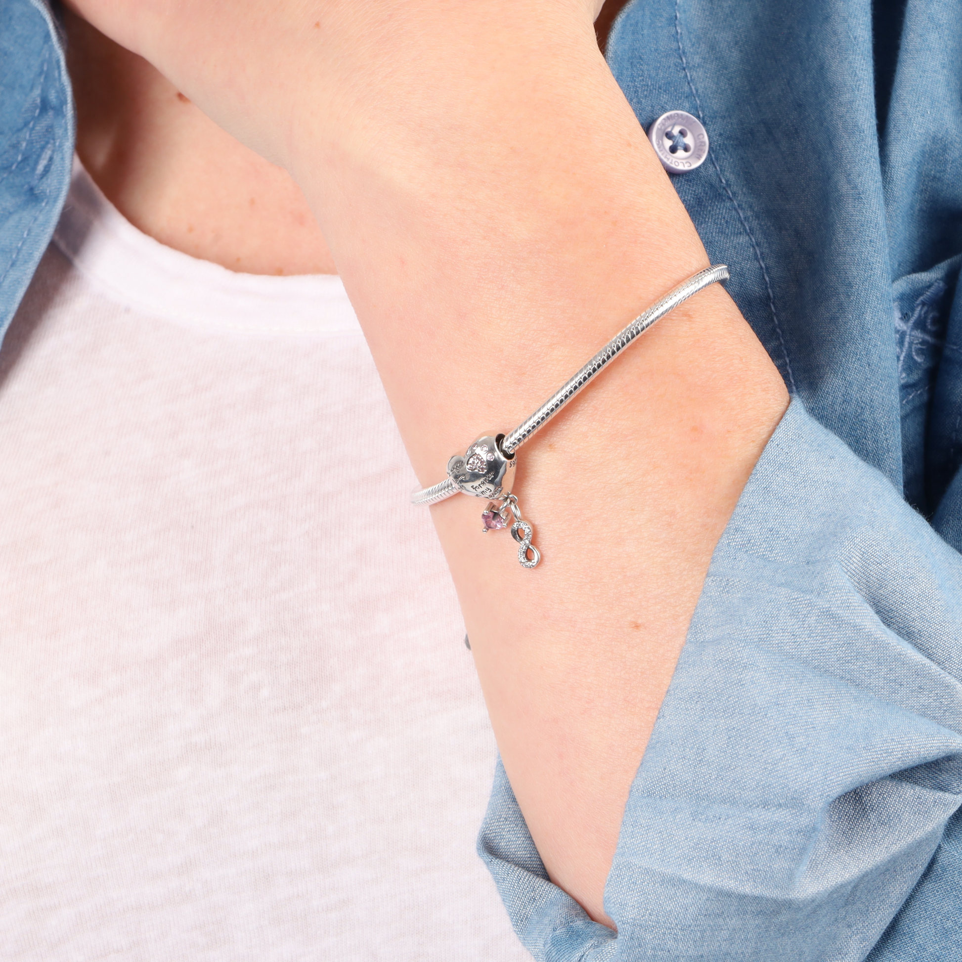 A person wearing the Mia Ishaaq Snake Chain Charm Bracelet, adorned with a small heart charm and vibrant stones on their wrist.