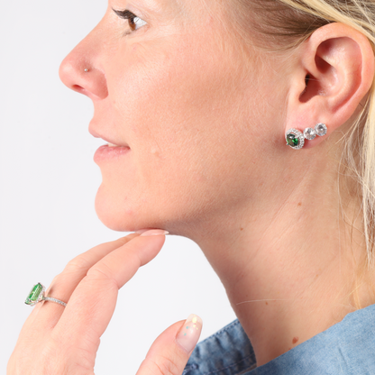 Person with green cubic zirconia stone earrings and a Crushed Ice Green Radiant Promise Ring by Mia Ishaaq, wearing a blue top, looking to the side.