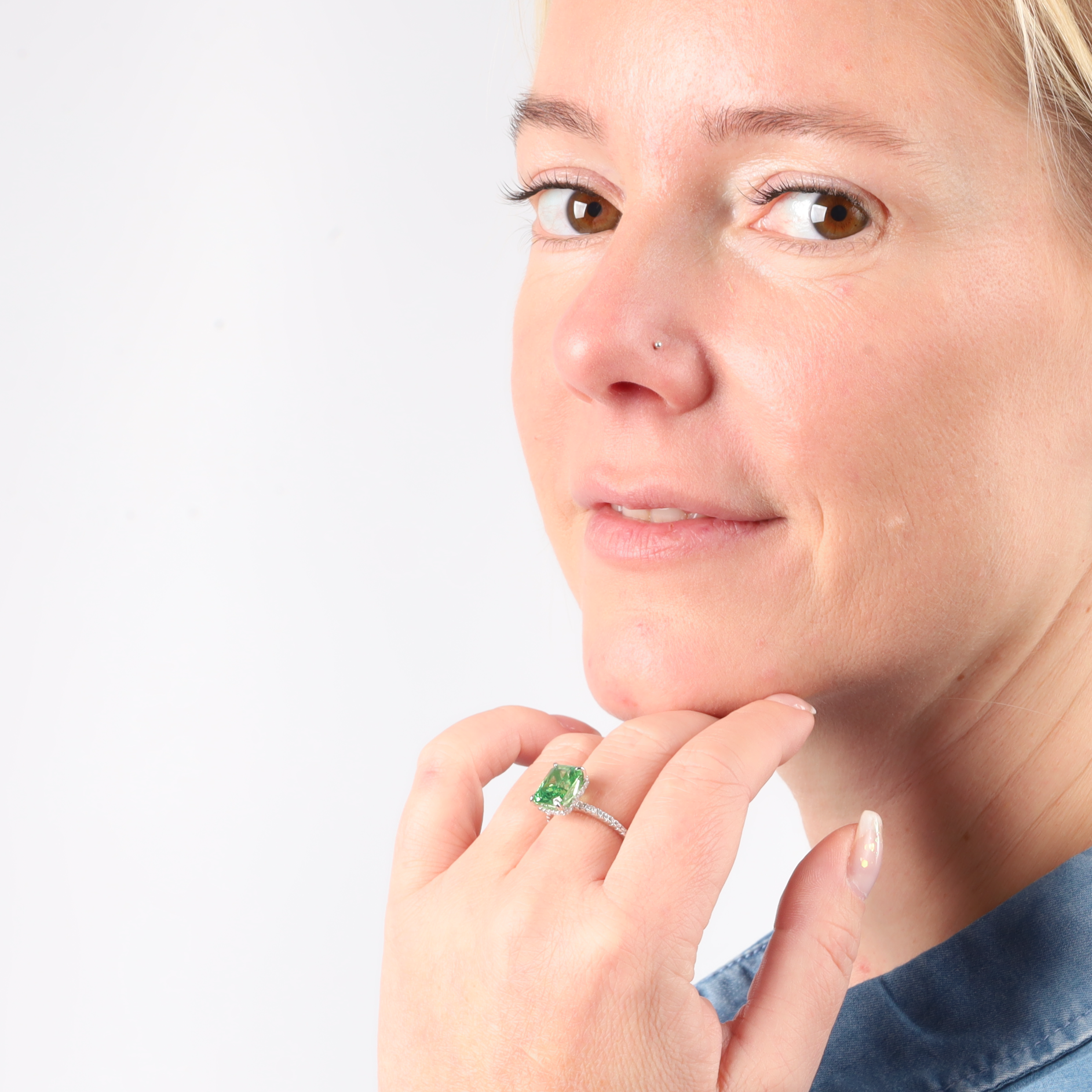 A woman wearing a Crushed Ice Green Radiant Promise Ring by Mia Ishaaq smiles slightly, posing in front of a plain white background.