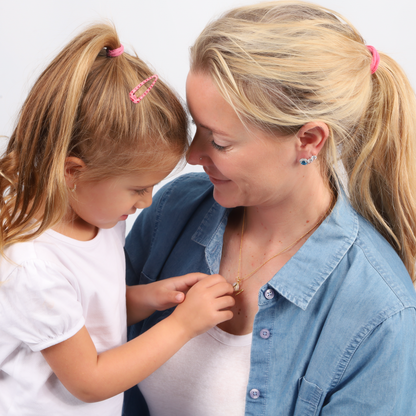 A mother and daughter beamed with joy as the child touched the Gold Vermeil Pearl Pendant Initial Necklace by Mia Ishaaq, featuring a delicate pearl pendant.