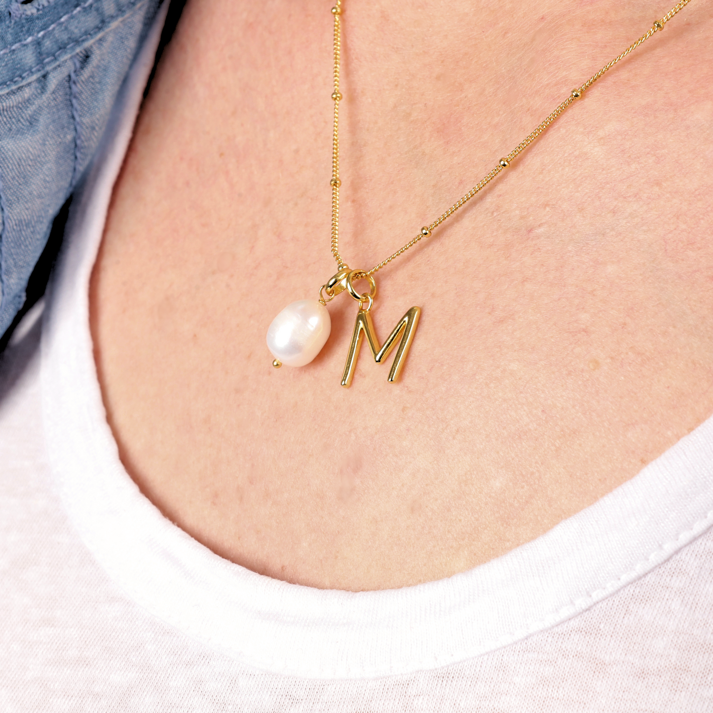 The elegant Gold Vermeil Pearl Pendant Initial Necklace by Mia Ishaaq on a model's neck with a personalized letter M pendant, featuring a radiant pearl.