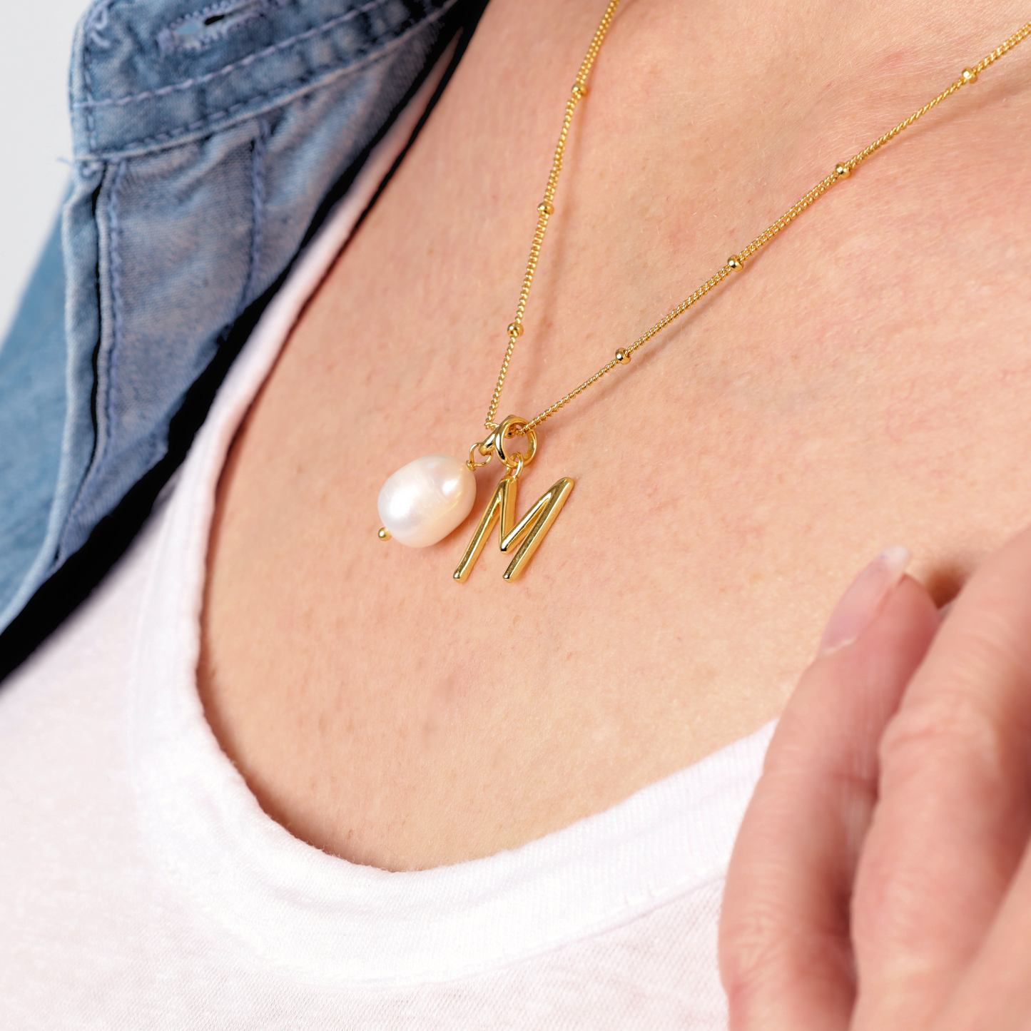 A stunning Gold Vermeil Pearl Pendant Initial Necklace by Mia Ishaaq featuring an "M" charm gracefully adorns a crisp white shirt.