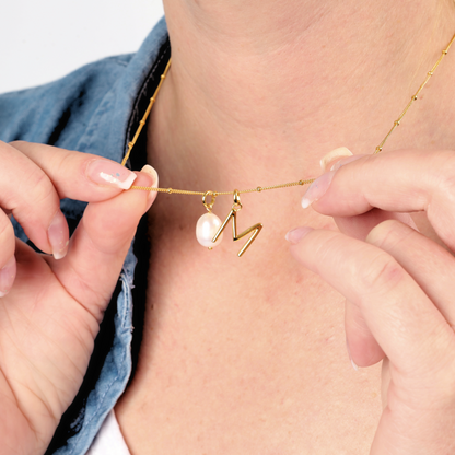 Model holding the Mia Ishaaq gold initial letter pearl pendant necklace between her fingers.