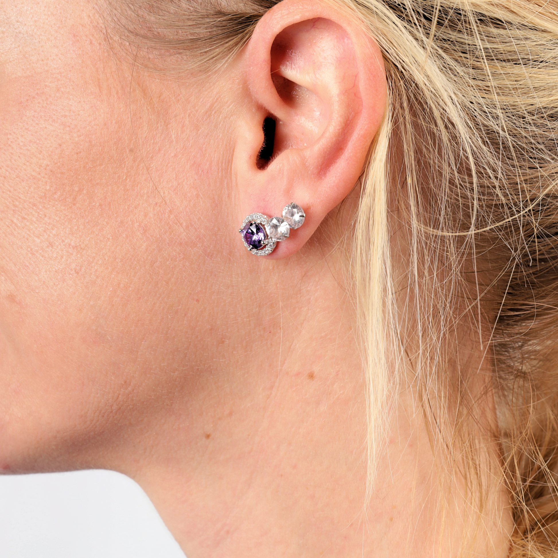 Close-up of a woman's ear adorned with a beautiful pair of Mia Ishaaq's 925 Sterling Silver VIOLET CZ Stud Earrings, her blonde hair elegantly pulled back.