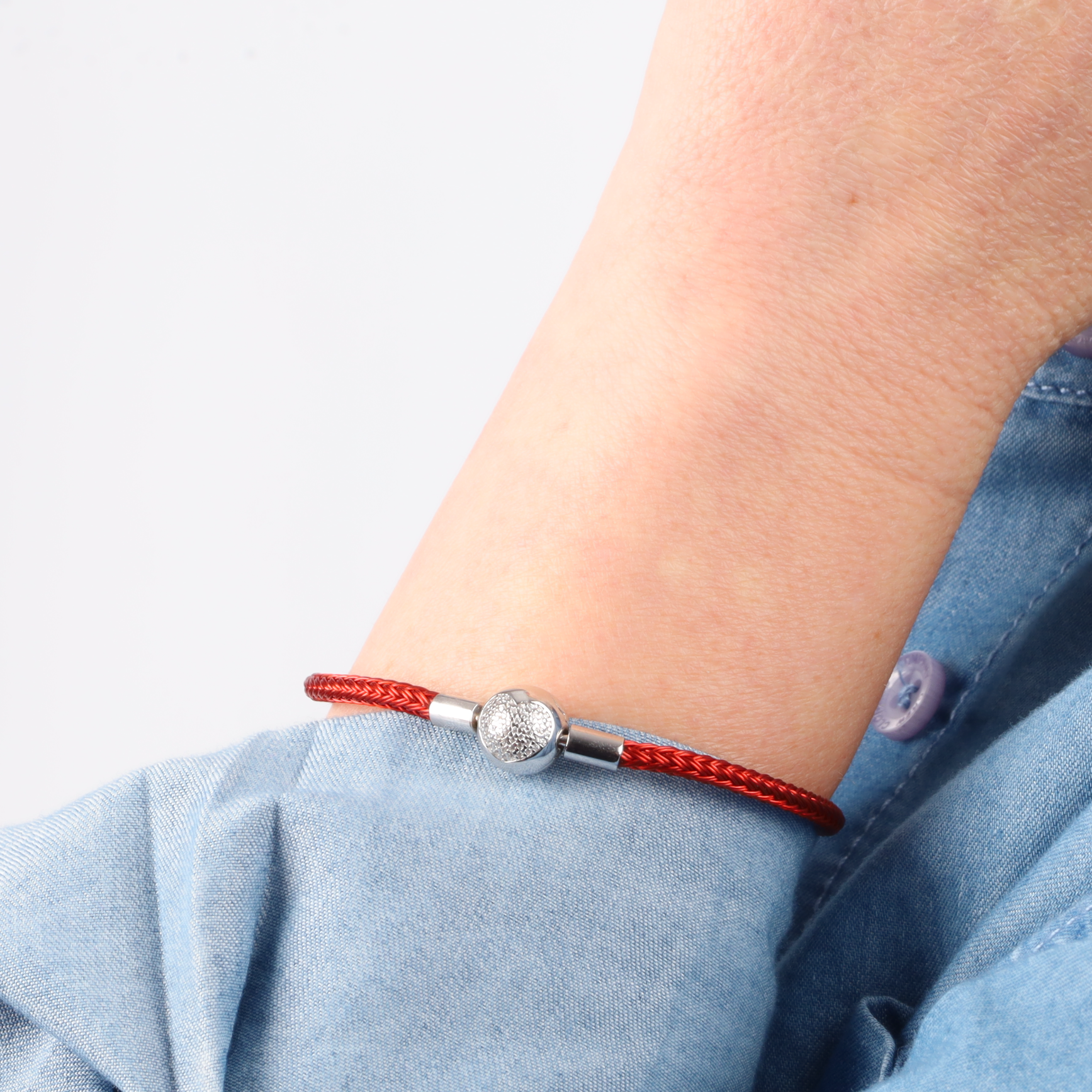 A person wearing the ATHENAIE "Heart of Fire Braided Charm Bracelet" featuring a 925 sterling silver clasp on their wrist.