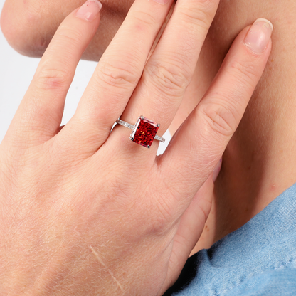 A hand showcases a Sterling Silver Red Radiant Ring by Mia Ishaaq, featuring a large, square red simulant stone.