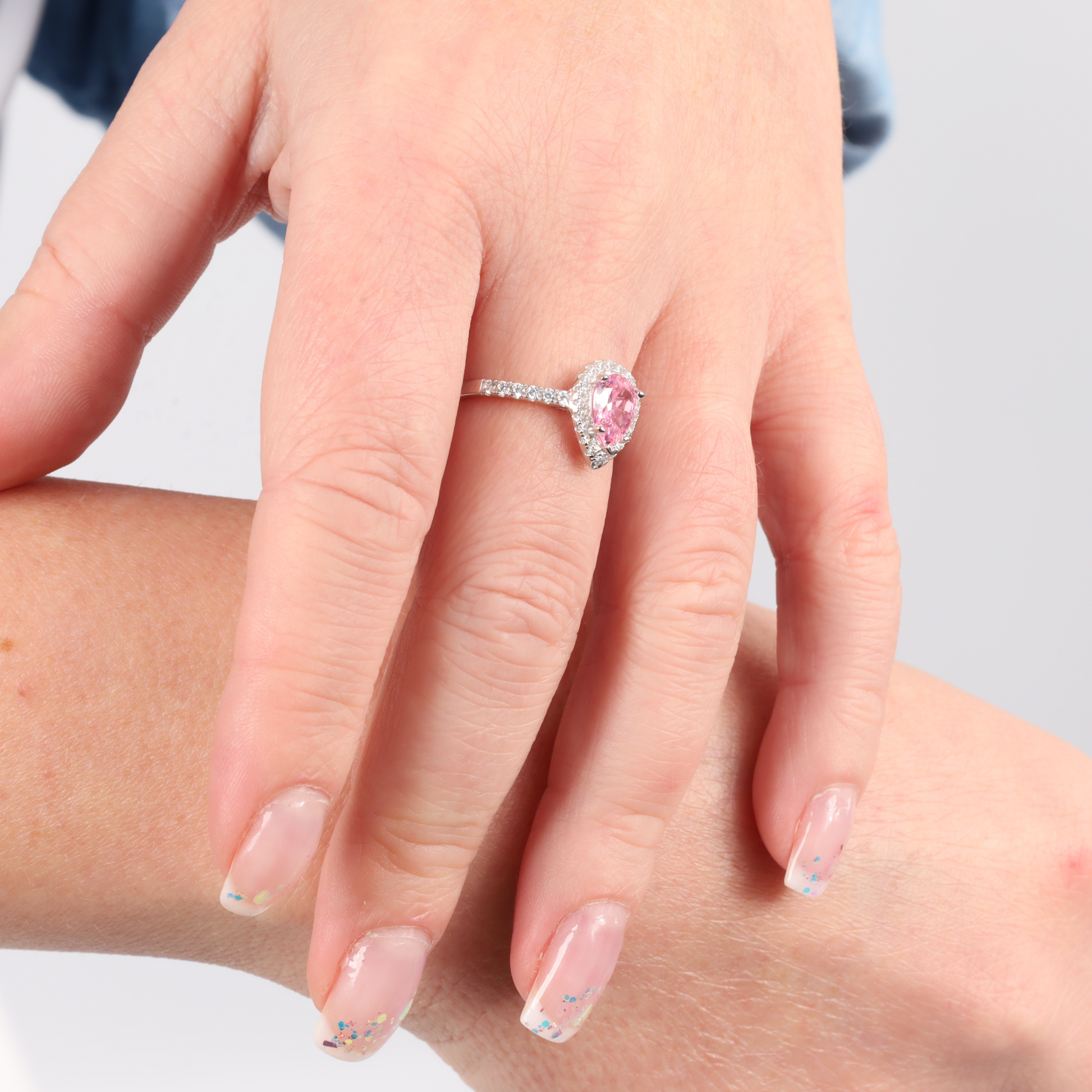 Close-up of a hand wearing the Mia Ishaaq Sterling Silver Drop HALO Ring, showcasing a teardrop-shaped pink CZ stone encircled by a diamond band.