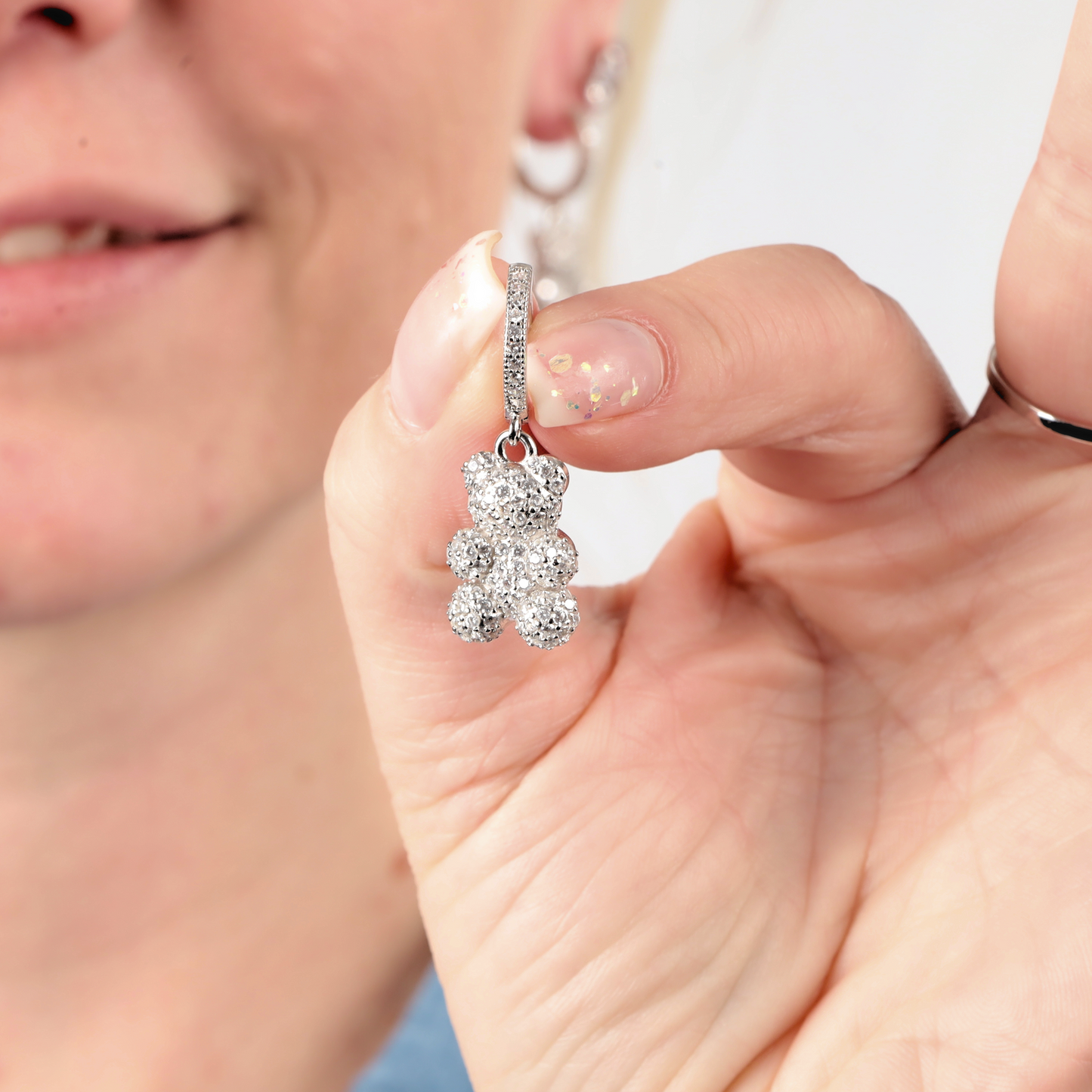 Close-up of a person holding a sparkly teddy bear-shaped earring between their fingers, crafted from sterling silver with dazzling cubic zirconia accents. The earring is one of the Pave Nostalgia Teddy Bear Earrings by Mia Ishaaq.