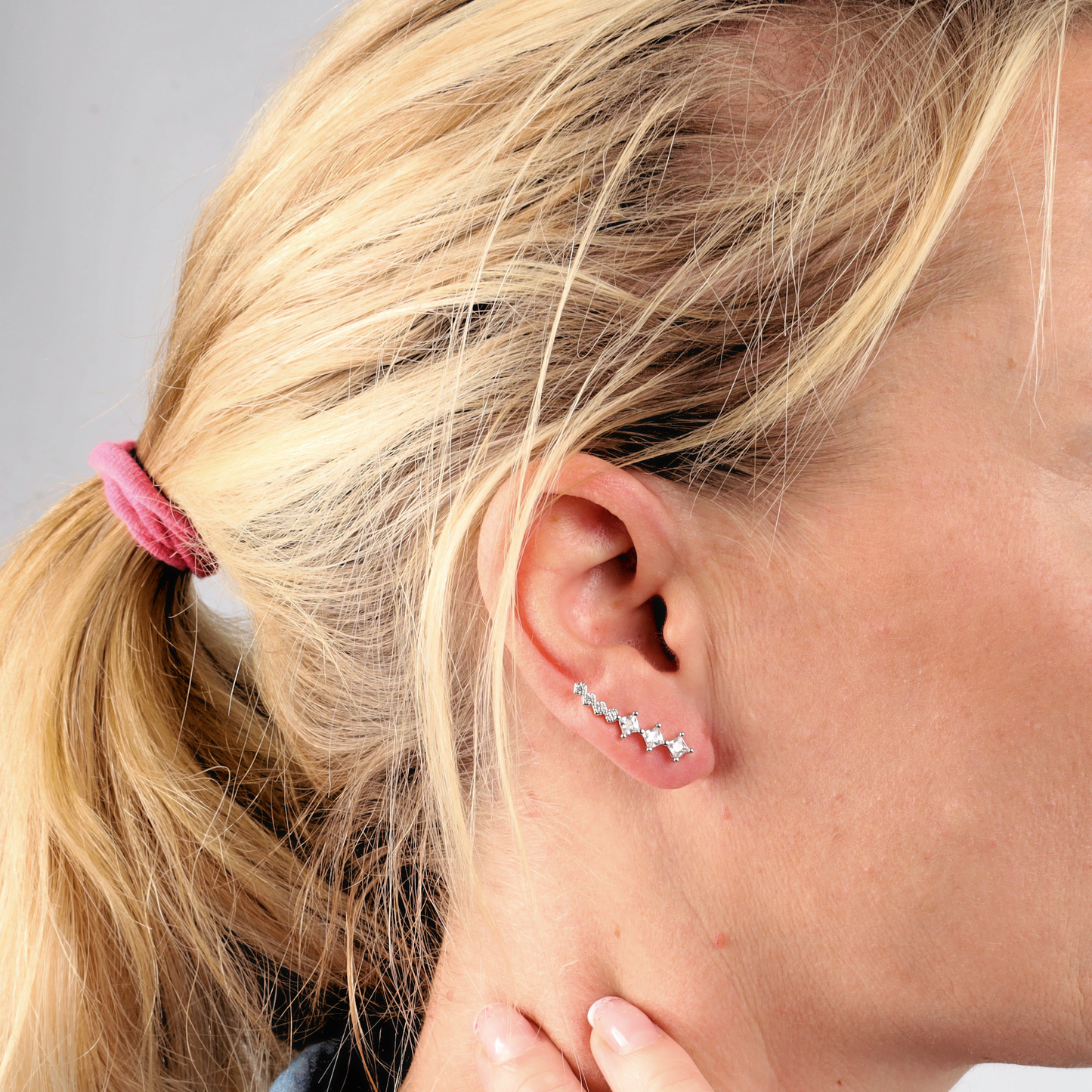 A woman with blonde hair in a ponytail wears Mia Ishaaq's Crystal Ear Cuffs Earrings, her hand gently touching her neck.