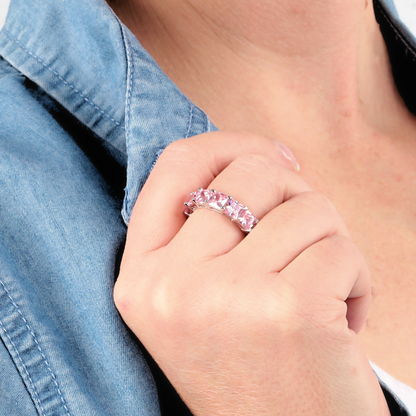 A person wearing a denim shirt displays a hand adorned with the Sterling Silver Pink Wide Band Ring by Mia Ishaaq, featuring a striking pink simulant stone.
