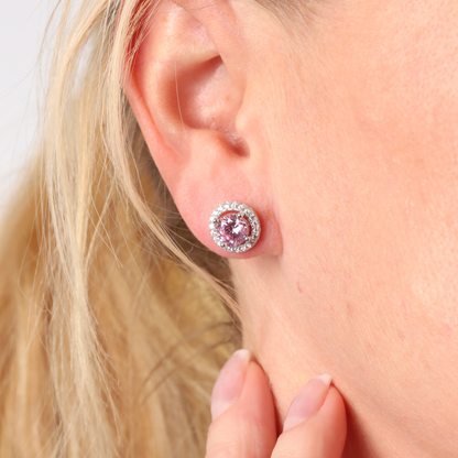 A close-up shot showcases a woman's ear wearing the exquisite Mia Ishaaq 925 Sterling Silver PINK CZ Stud Earrings, highlighting their circular pink cubic zirconia center with a dazzling halo design.