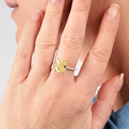 Close-up of a hand adorned with a Mia Ishaaq Crushed Ice Yellow Radiant Promise Ring on the ring finger, its brilliance enhanced by the delicate white gold plated band, set against a light background.