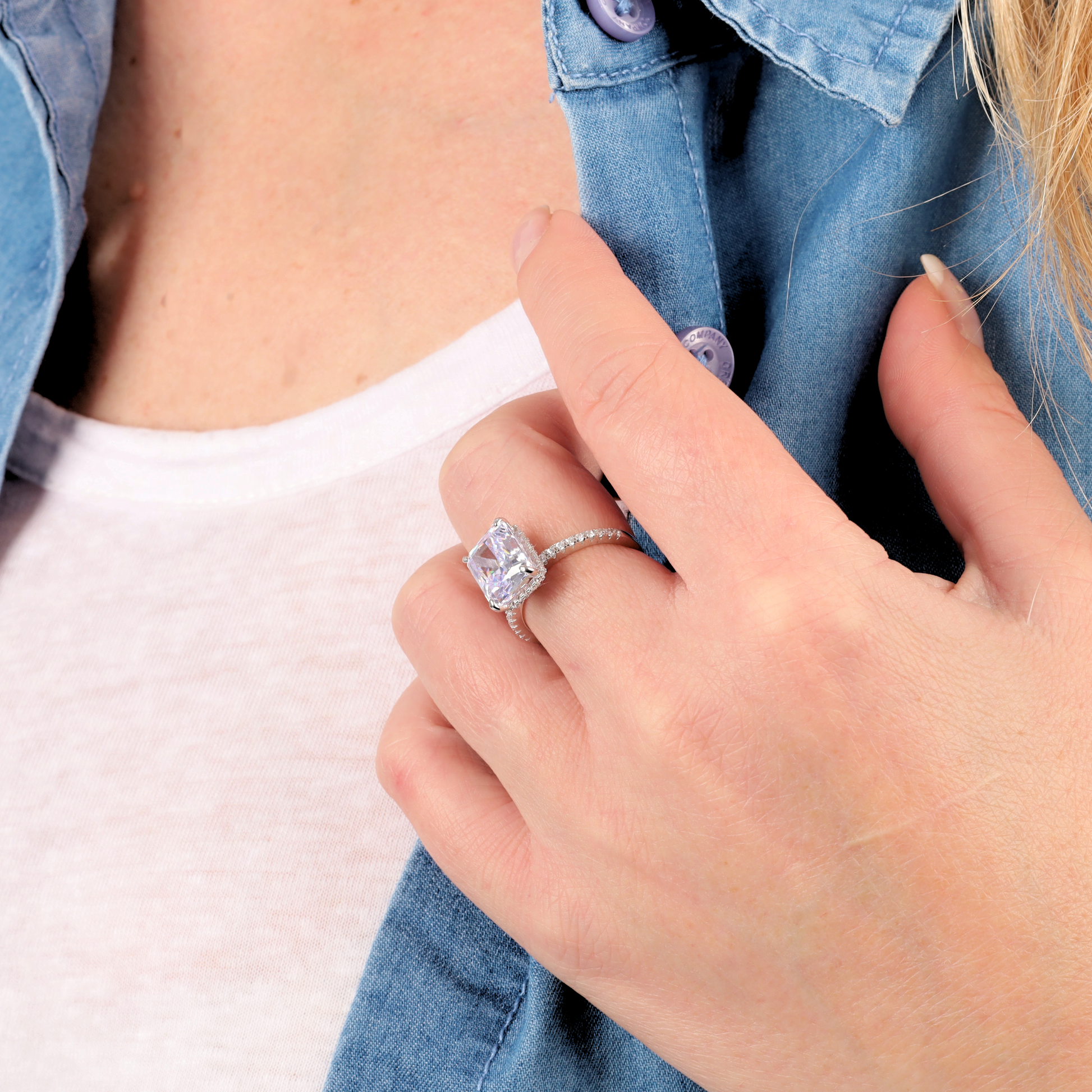 A person wearing a Mia Ishaaq Crushed Ice Lilac Radiant Promise Ring on their finger, touching the collar of a blue denim shirt over a white top.