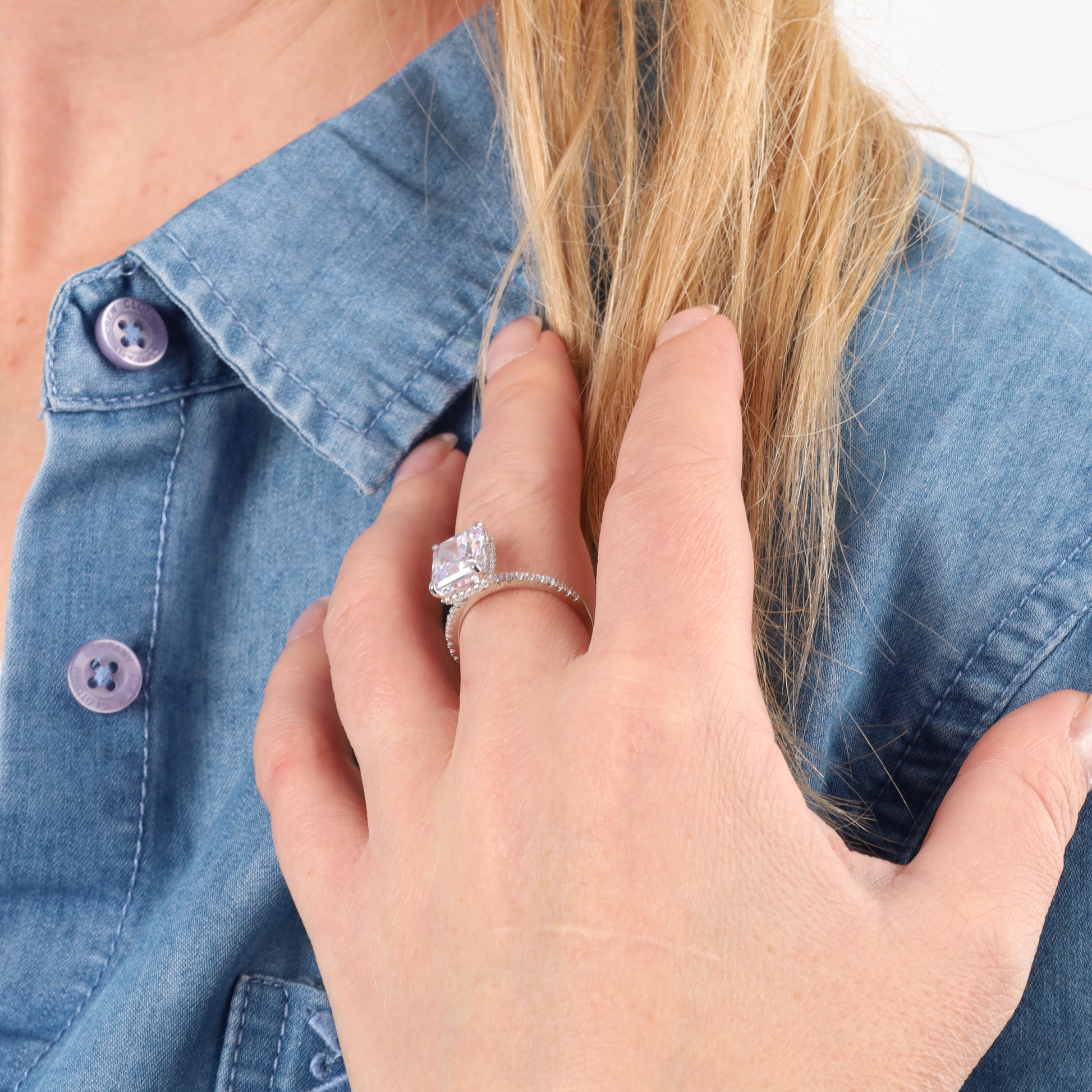 A woman in a denim shirt displays her Crushed Ice Lilac Radiant Promise Ring from Mia Ishaaq, gracefully holding her blond hair.