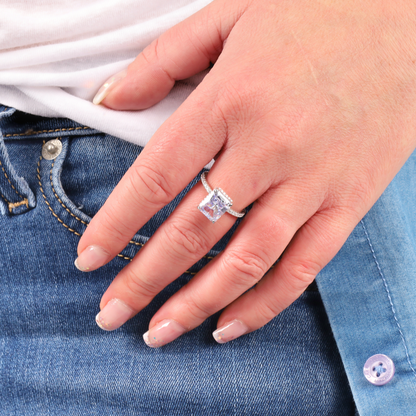 A hand adorned with a Mia Ishaaq Crushed Ice Lilac Radiant Promise Ring rests elegantly on denim jeans, capturing the perfect blend of casual style and timeless elegance.