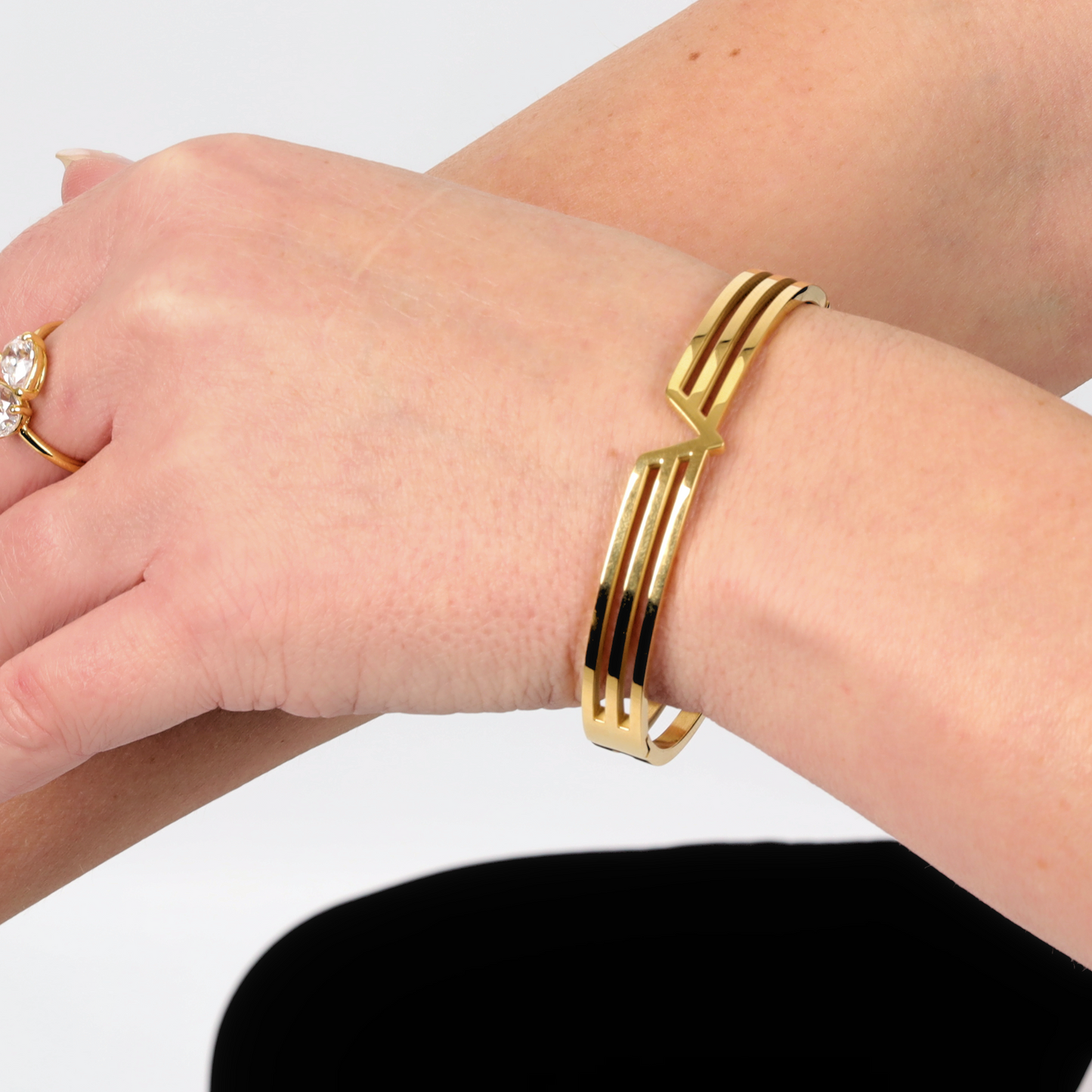 A Gold V Line Harmony Bangle Bracelet by Mia Ishaaq, featuring a graceful zigzag design, elegantly encircles model's wrist.