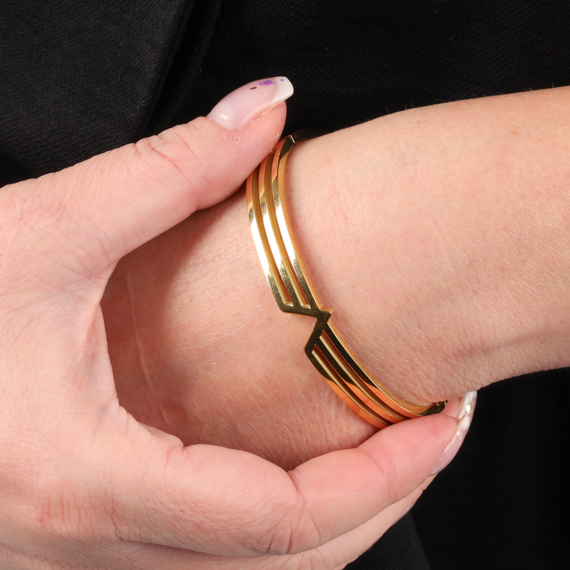 A hand elegantly showcases the sleek minimalist Gold V Line Harmony Bangle Bracelet by Mia Ishaaq on the wrist.