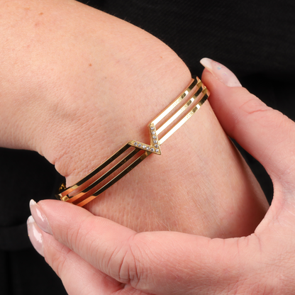 Close-up of a hand adjusting the Mia Ishaaq® Gold Crystal V Line Harmony Bangle, a stunning piece featuring a V-shaped design embellished with small crystals and elegantly crafted with 18k gold plating.