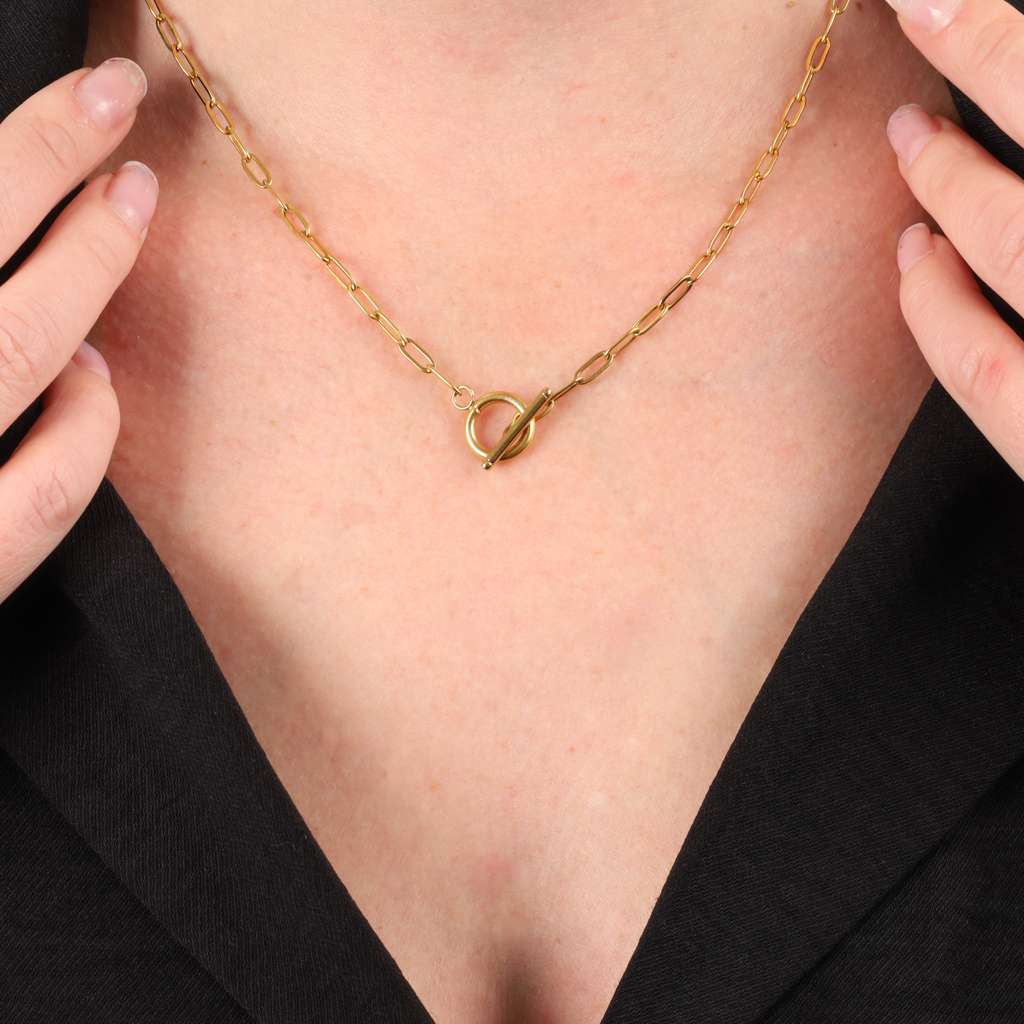 A person wearing the Mia Ishaaq Link Chain T-Bar Layering Necklace in 18k gold-plating, with hands at the neckline of a black top.