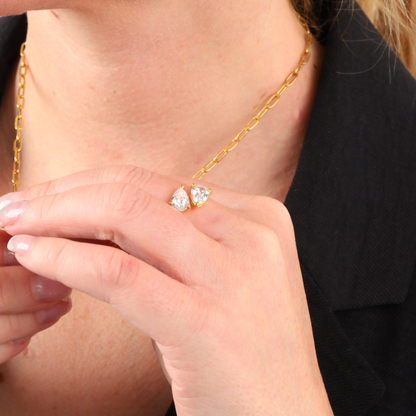 A person wearing a 14k gold plated chain necklace and holding the Gold Twist Teardrop Ring by Mia Ishaaq, crafted in sterling silver and adorned with two large, teardrop cubic zirconia gemstones.