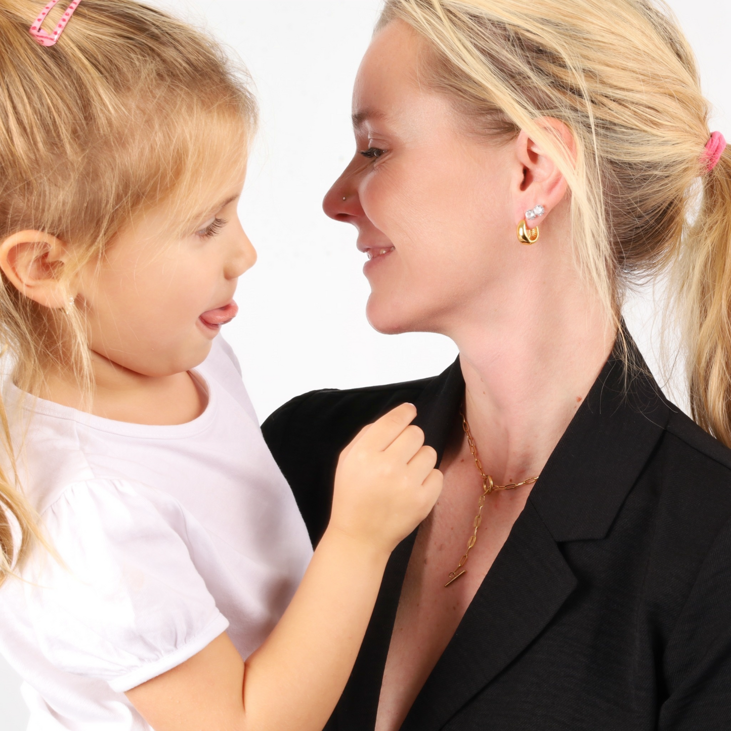 A woman and a young girl share a joyful moment, facing each other and smiling warmly, their laughter enhanced by glimmers from the woman's Mia Ishaaq® Gold Crystal Hoop Earrings.