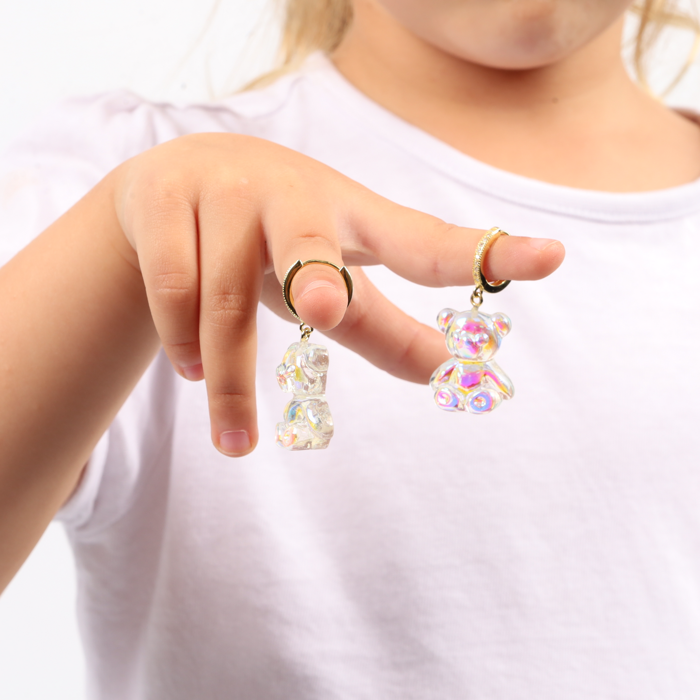 A child holds two crystal teddy bear keychains with gold rings, reminiscent of Mia Ishaaq's Shimmering Teddy Bear Earrings adorned with shimmering elegance.