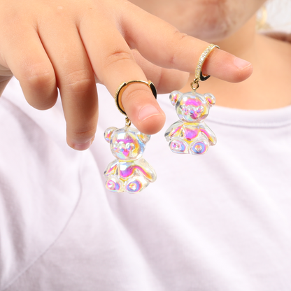 A close-up view of a person wearing the Shimmering Teddy Bear Earrings by Mia Ishaaq, crafted from cubic zirconia, against a white shirt.