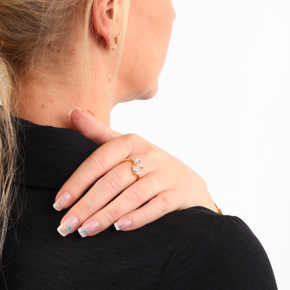 Close-up of a person touching their neck, showcasing the Gold Twist Teardrop Ring by Mia Ishaaq, featuring a teardrop cubic zirconia set in 14k gold plating, accentuated by manicured nails.