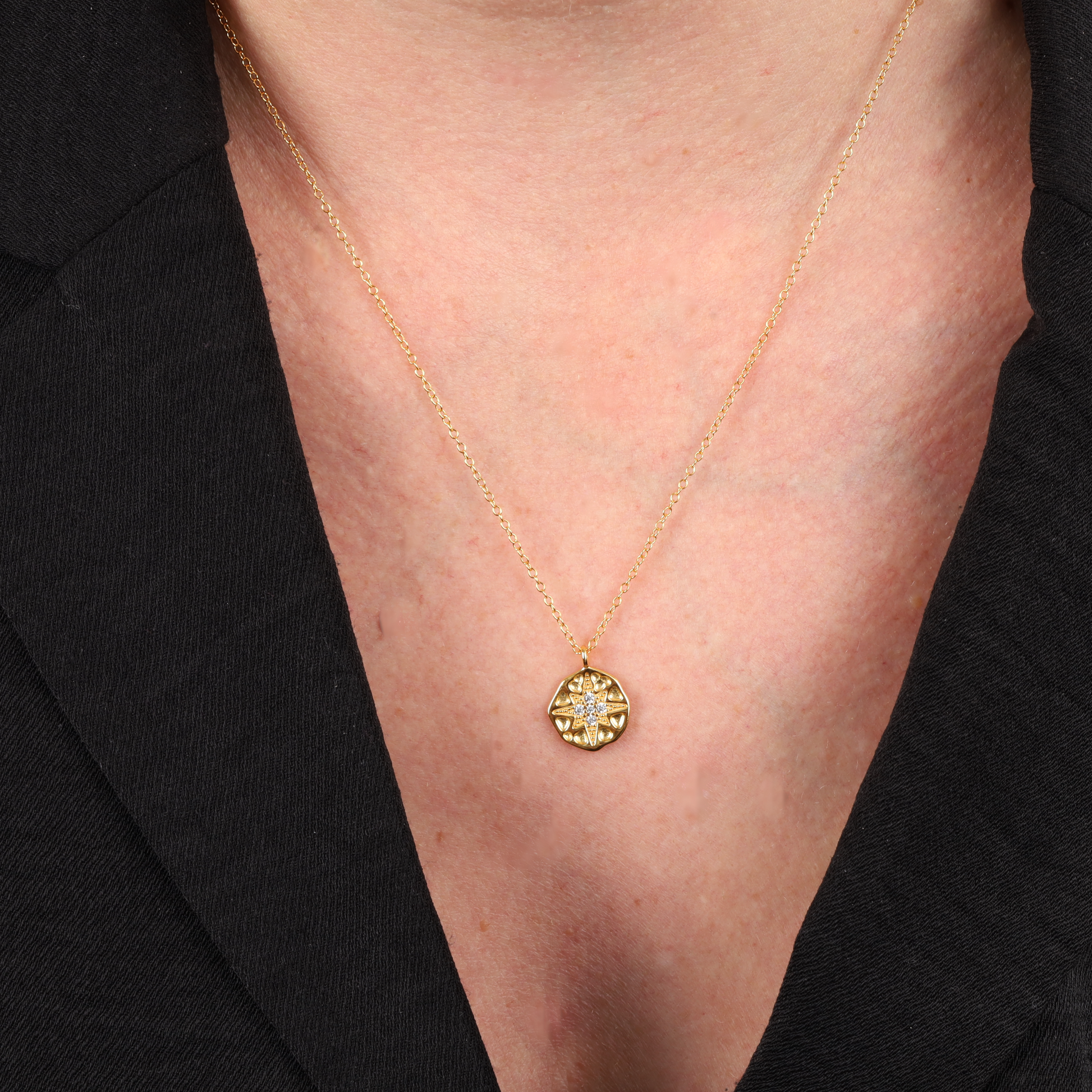 A close-up of Mia Ishaaq®'s Polaris Coin Pendant Necklace in gold, showcasing its celestial-inspired North Star pendant with a sparkling gemstone, elegantly worn over a black shirt.