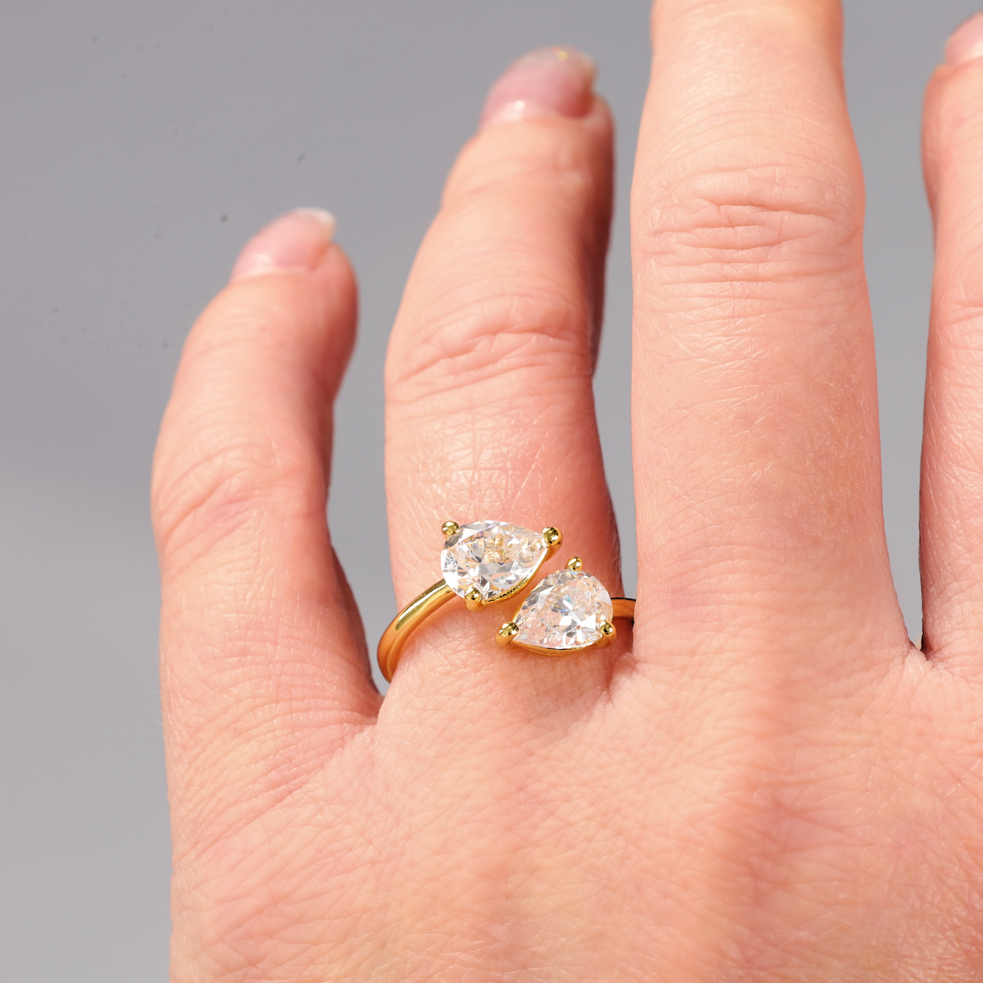 A hand adorned with the Gold Twist Teardrop Ring by Mia Ishaaq, featuring a stunning 14k gold-plated design and two teardrop cubic zirconia stones on the ring finger.